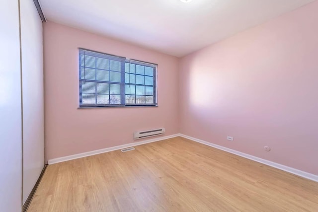 unfurnished room featuring light wood finished floors, visible vents, a baseboard heating unit, and baseboards