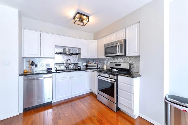 kitchen featuring a sink, appliances with stainless steel finishes, white cabinets, light wood finished floors, and decorative backsplash