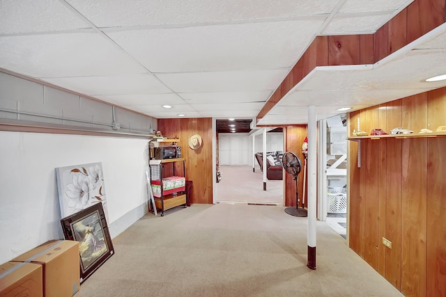 finished basement featuring a paneled ceiling, wood walls, and carpet flooring