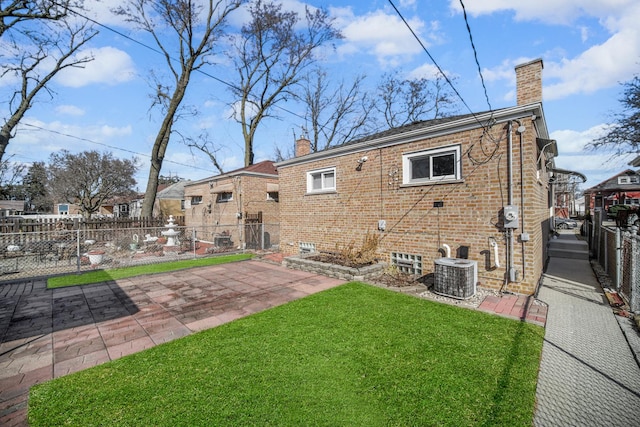 rear view of property with fence, central air condition unit, a lawn, a chimney, and a patio