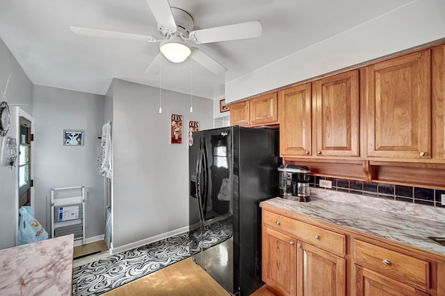 kitchen featuring brown cabinets, a ceiling fan, backsplash, light countertops, and black refrigerator with ice dispenser