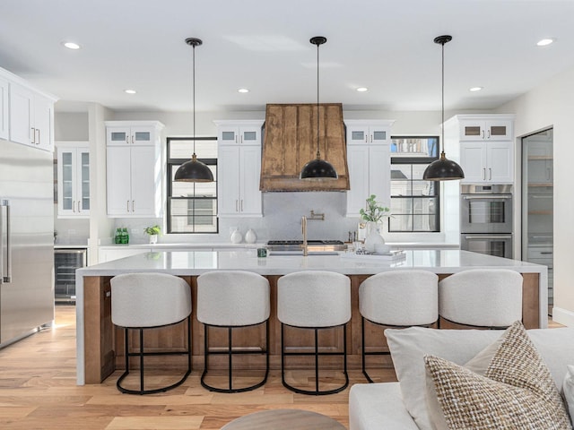 kitchen with a spacious island, stainless steel appliances, light countertops, custom range hood, and light wood-type flooring