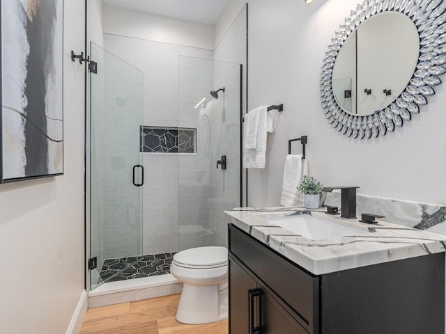 full bath with toilet, a stall shower, wood finished floors, baseboards, and vanity