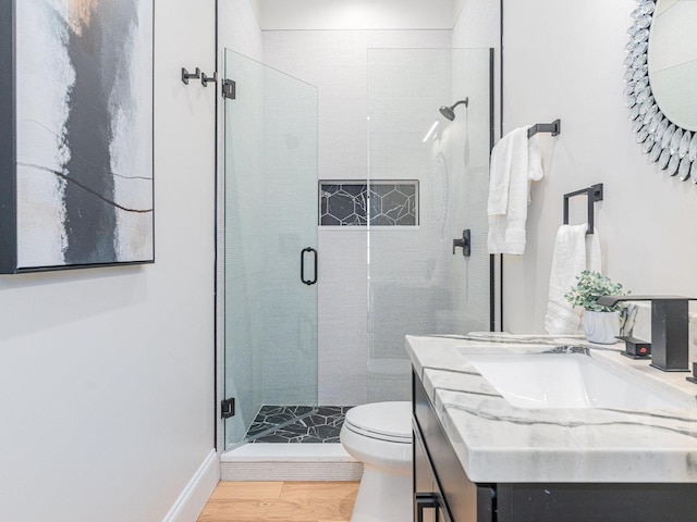 bathroom with a shower stall, toilet, vanity, and wood finished floors