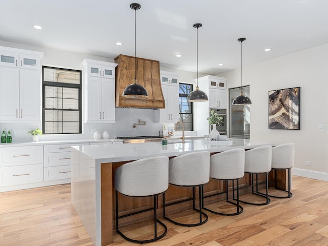 kitchen featuring a sink, decorative backsplash, a spacious island, and light wood finished floors