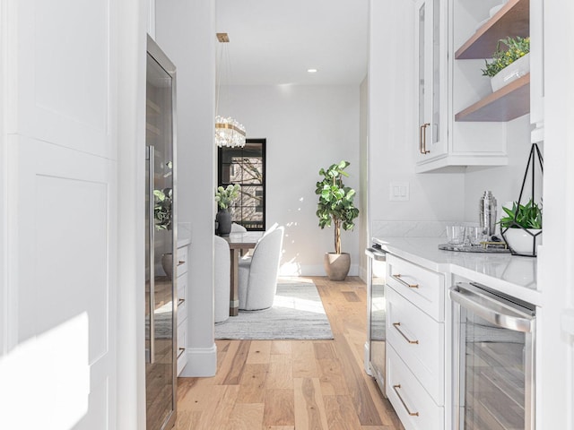 interior space with baseboards, light wood-style flooring, recessed lighting, wine cooler, and a chandelier