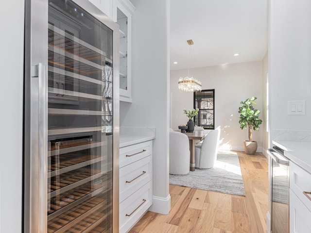 interior space with wine cooler, a chandelier, white cabinets, and light wood-type flooring