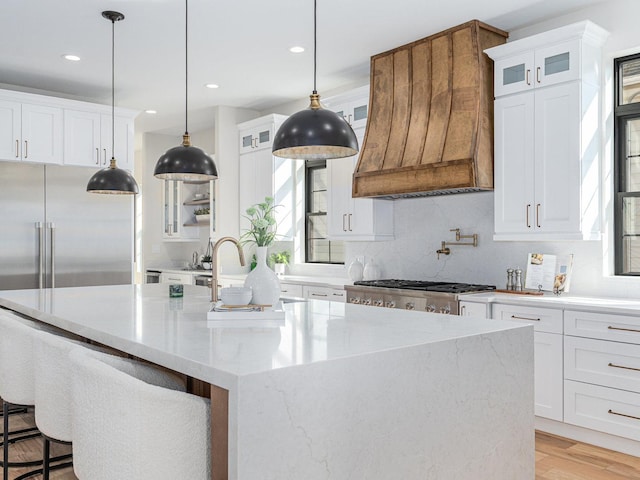 kitchen with a kitchen island with sink, premium range hood, light wood-style floors, white cabinetry, and range