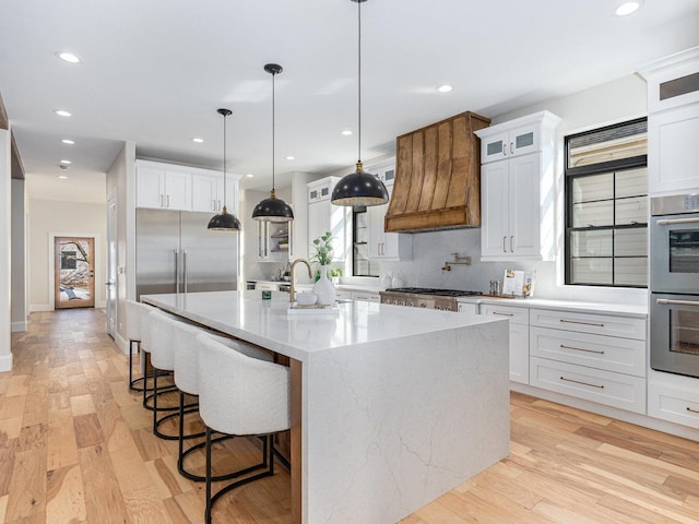 kitchen with custom range hood, light wood-style floors, a large island, stainless steel appliances, and a sink