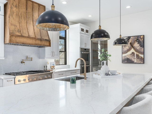 kitchen with light stone counters, stainless steel appliances, a sink, custom range hood, and glass insert cabinets