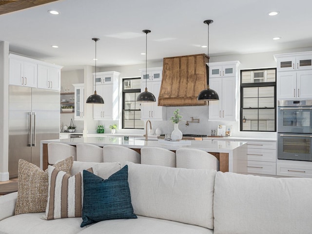 kitchen with premium range hood, open floor plan, white cabinetry, stainless steel appliances, and light countertops