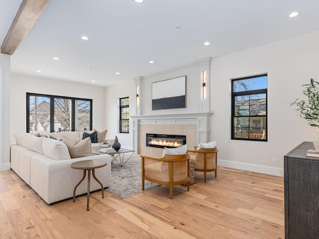 living room featuring recessed lighting, a glass covered fireplace, light wood-style flooring, and baseboards