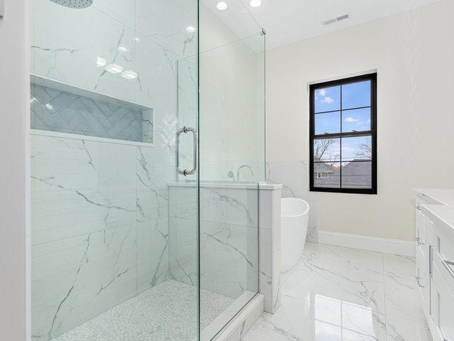 bathroom with a marble finish shower, marble finish floor, a freestanding bath, and baseboards