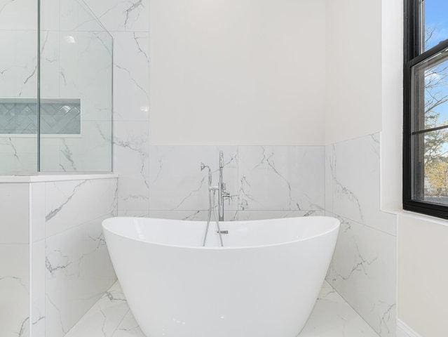 bathroom with marble finish floor and a freestanding bath