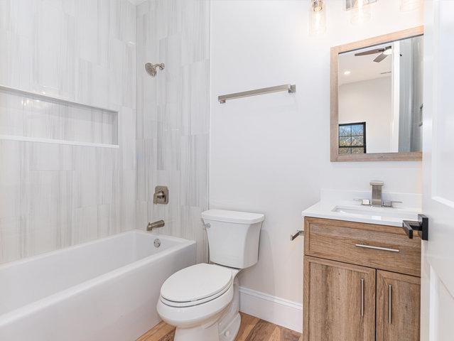 bathroom featuring vanity, wood finished floors, baseboards,  shower combination, and toilet