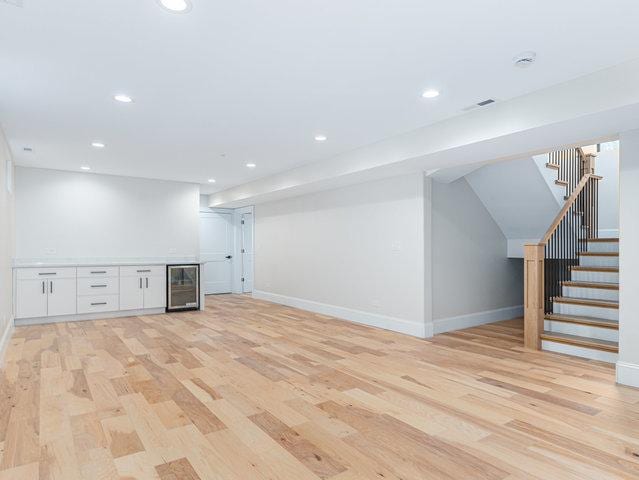 basement with a bar, stairway, wine cooler, and light wood-style flooring