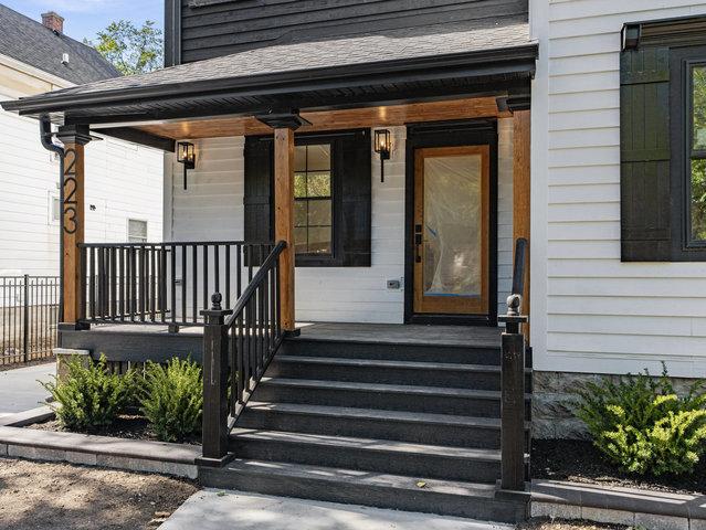 doorway to property with a porch, fence, and a shingled roof