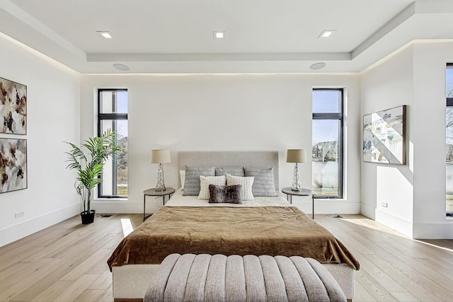 bedroom with a tray ceiling, light wood-type flooring, and baseboards