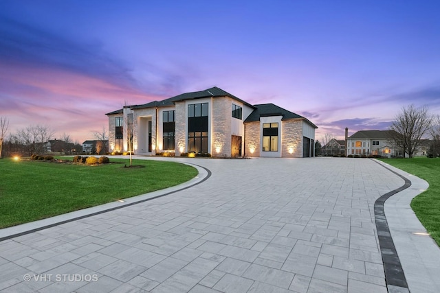 view of front of home featuring stucco siding, decorative driveway, stone siding, and a yard