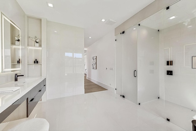 bathroom with a shower with door, double vanity, tile walls, and a sink