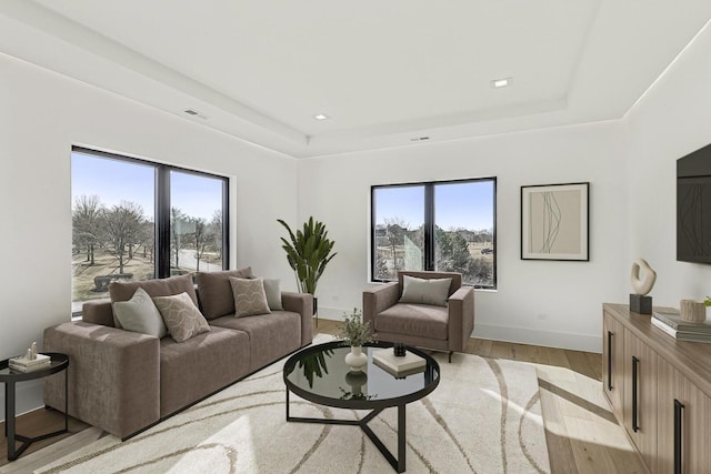 living area featuring a tray ceiling, light wood-style flooring, visible vents, and baseboards