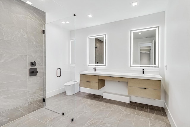 full bath featuring baseboards, toilet, double vanity, a stall shower, and a sink