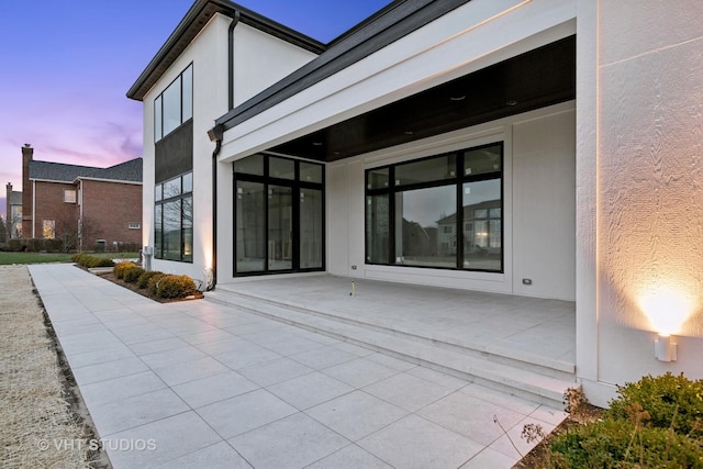 back of property at dusk featuring a patio and stucco siding