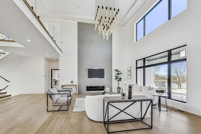 living area with light wood finished floors, visible vents, baseboards, stairway, and a high ceiling