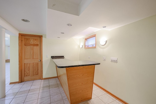 kitchen with light tile patterned floors, a peninsula, dark countertops, and baseboards