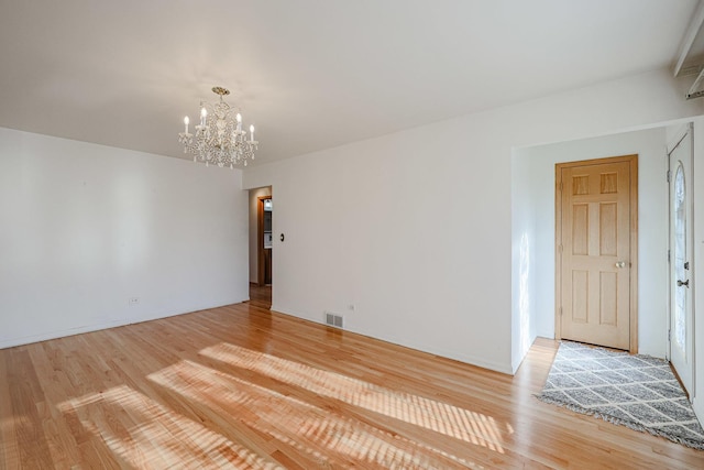 empty room featuring visible vents, a notable chandelier, and wood finished floors