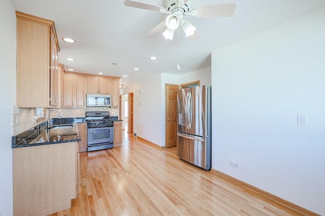 kitchen featuring light brown cabinetry, a sink, tasteful backsplash, appliances with stainless steel finishes, and light wood finished floors