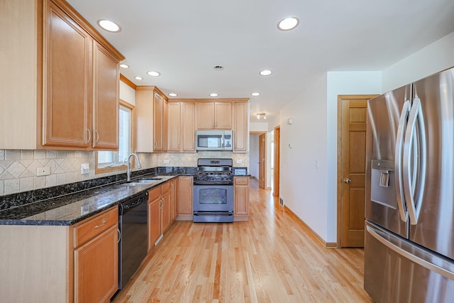 kitchen featuring a sink, dark stone countertops, appliances with stainless steel finishes, light wood finished floors, and decorative backsplash