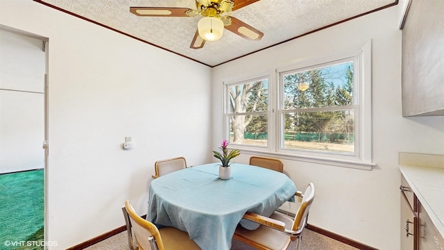 carpeted dining area with ceiling fan, baseboards, and ornamental molding