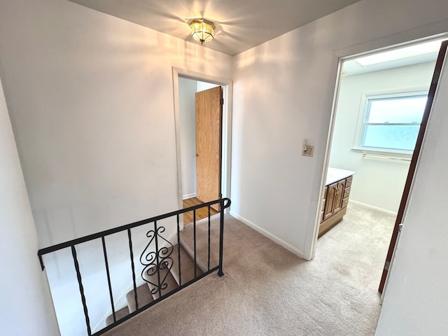 hall with an upstairs landing, baseboards, and light carpet