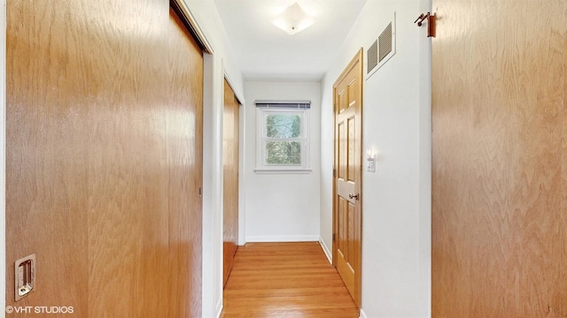 hall with baseboards, visible vents, and light wood finished floors