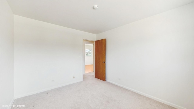 spare room with baseboards and light colored carpet