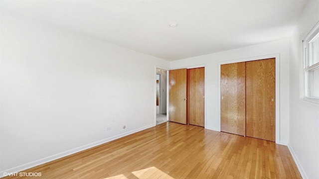 unfurnished bedroom with baseboards, multiple closets, and light wood-style flooring