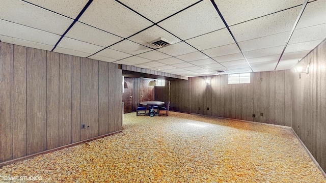 basement with a paneled ceiling, visible vents, carpet floors, and wood walls