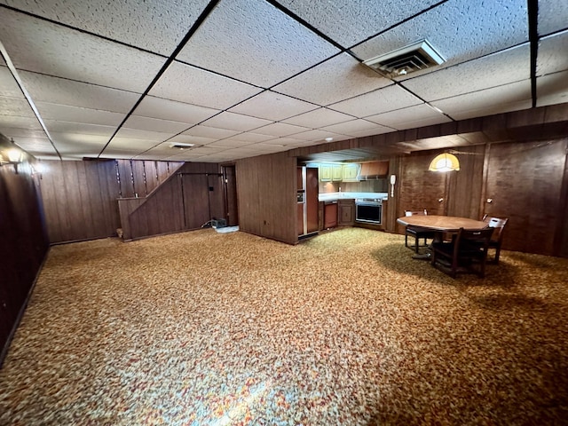 finished basement featuring a paneled ceiling, visible vents, wood walls, and light carpet