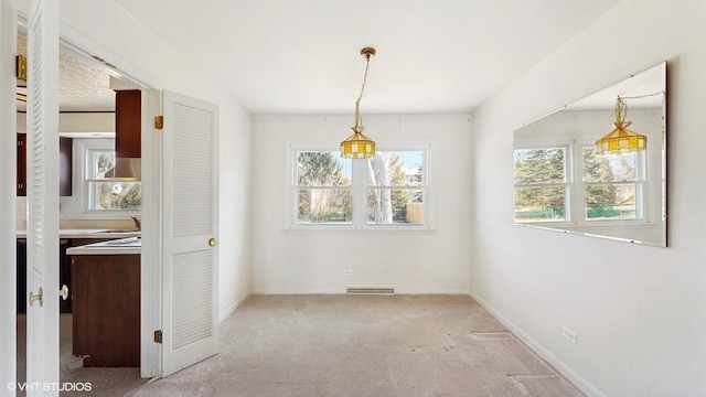 unfurnished dining area with carpet flooring, baseboards, visible vents, and a sink