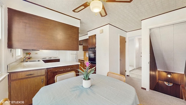 kitchen featuring light countertops, carpet floors, brown cabinets, a ceiling fan, and a sink