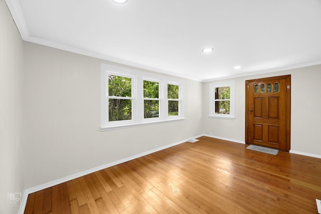 empty room with crown molding, light wood-style floors, baseboards, and visible vents