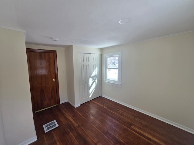 unfurnished bedroom featuring dark wood finished floors, visible vents, baseboards, and a closet