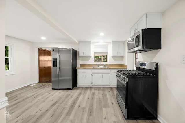 kitchen featuring light wood finished floors, baseboards, appliances with stainless steel finishes, white cabinetry, and a sink