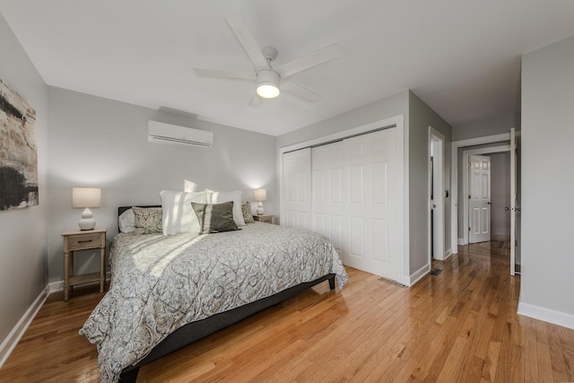 bedroom with a closet, wood-type flooring, baseboards, and a wall mounted AC