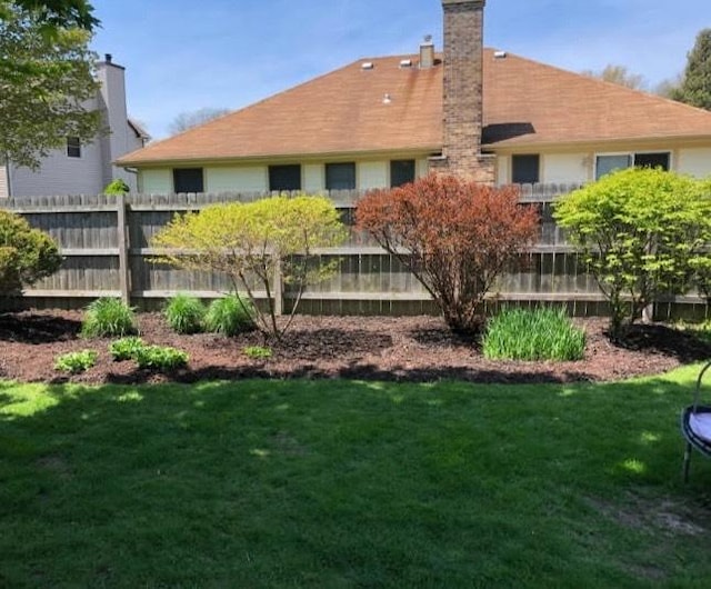 rear view of property with a chimney, a yard, and fence