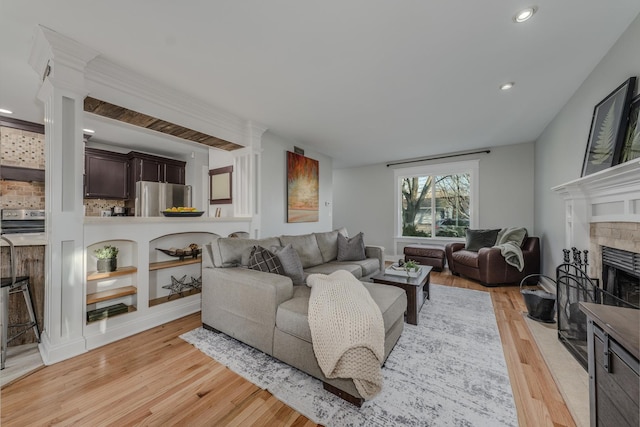 living area featuring a fireplace with flush hearth, light wood-style floors, recessed lighting, and decorative columns