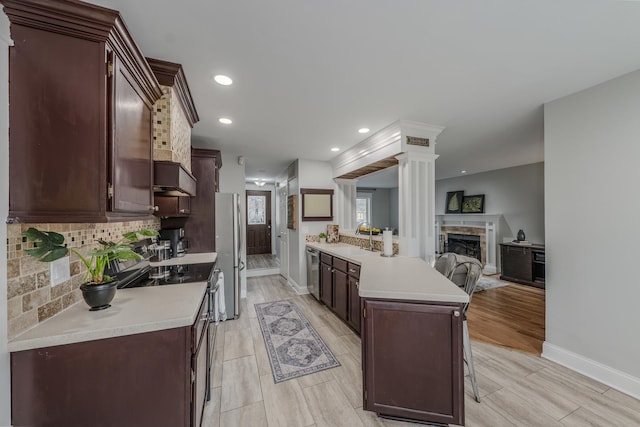 kitchen with tasteful backsplash, light countertops, a stone fireplace, appliances with stainless steel finishes, and a sink