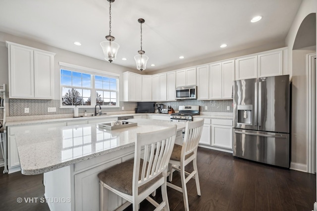 kitchen with a kitchen island, appliances with stainless steel finishes, dark wood-style floors, white cabinetry, and a sink