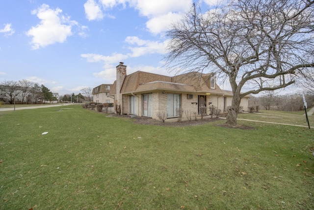 view of side of property with a shingled roof, a lawn, brick siding, and a chimney